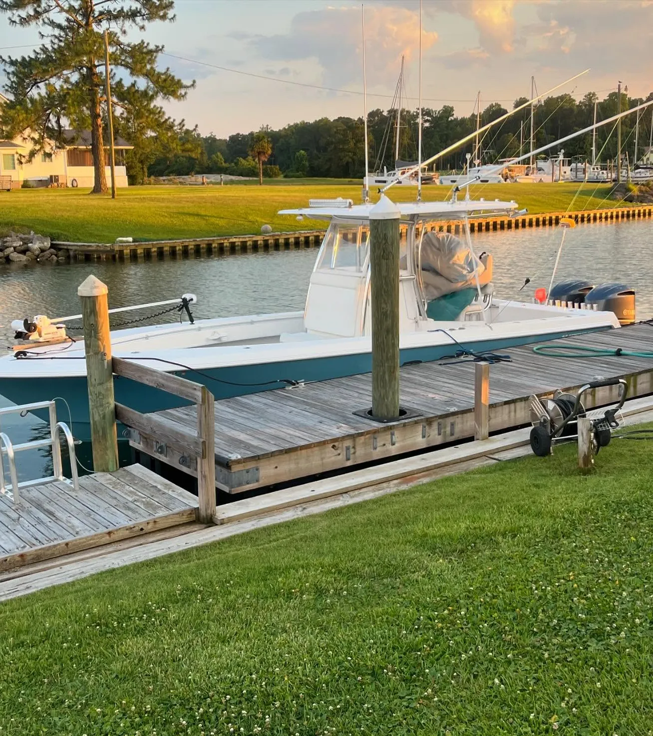 boat-1 A white boat is docked at a wooden pier along a grassy waterfront at sunset.