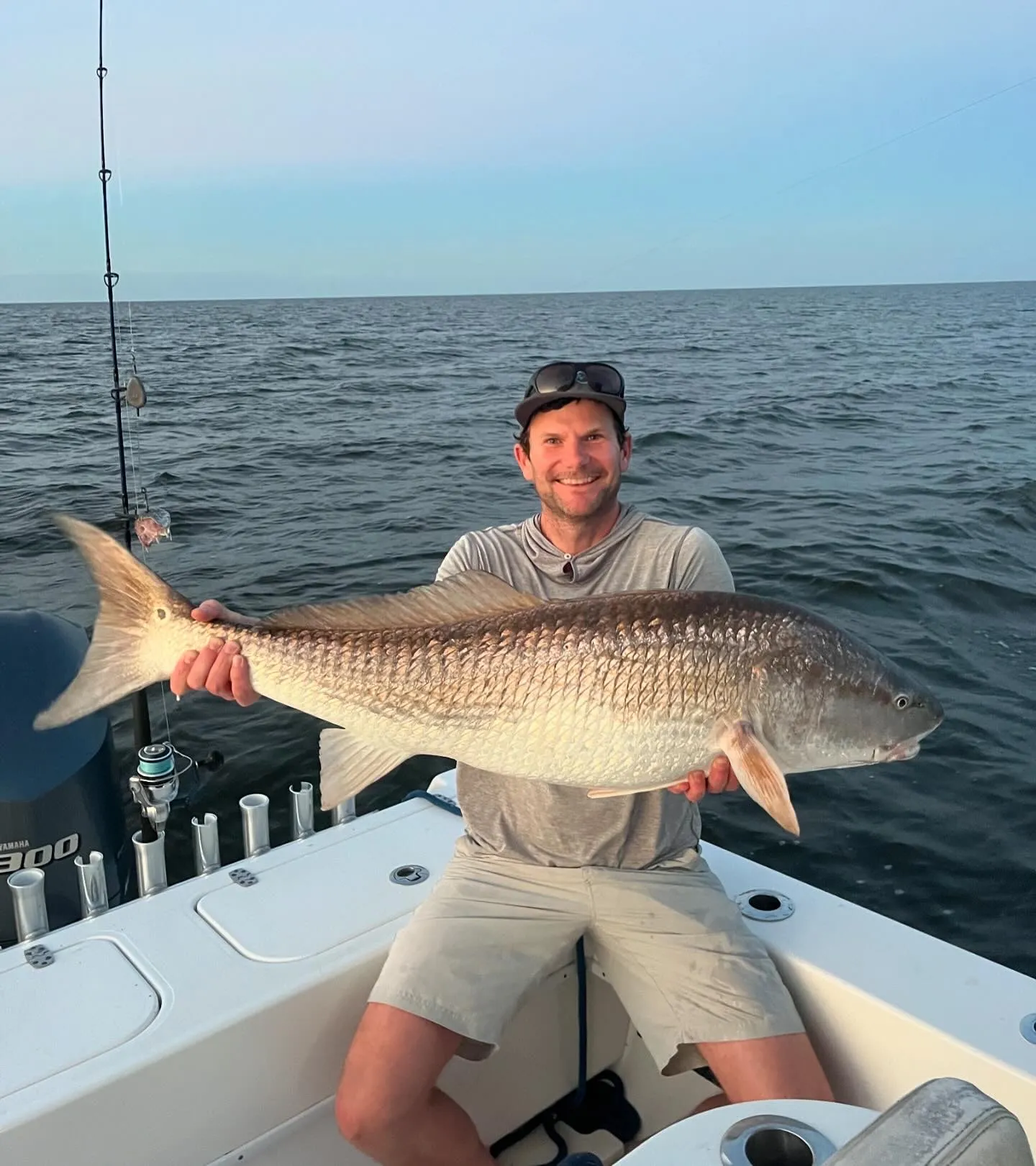 bottom-2 Man sitting on a boat holding a large fish with the ocean and sky in the background.