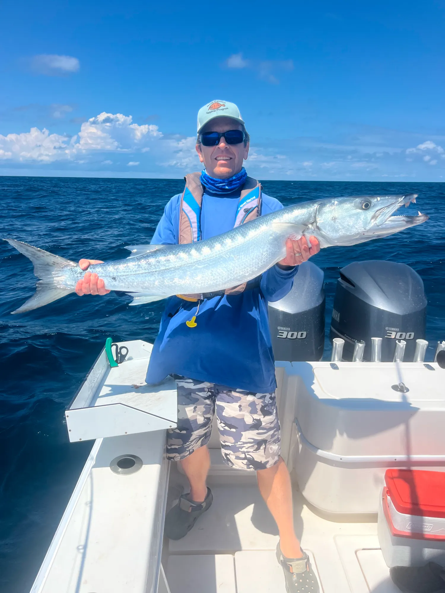 bottom-w Person on a boat holding a large barracuda fish with the ocean and sky in the background.