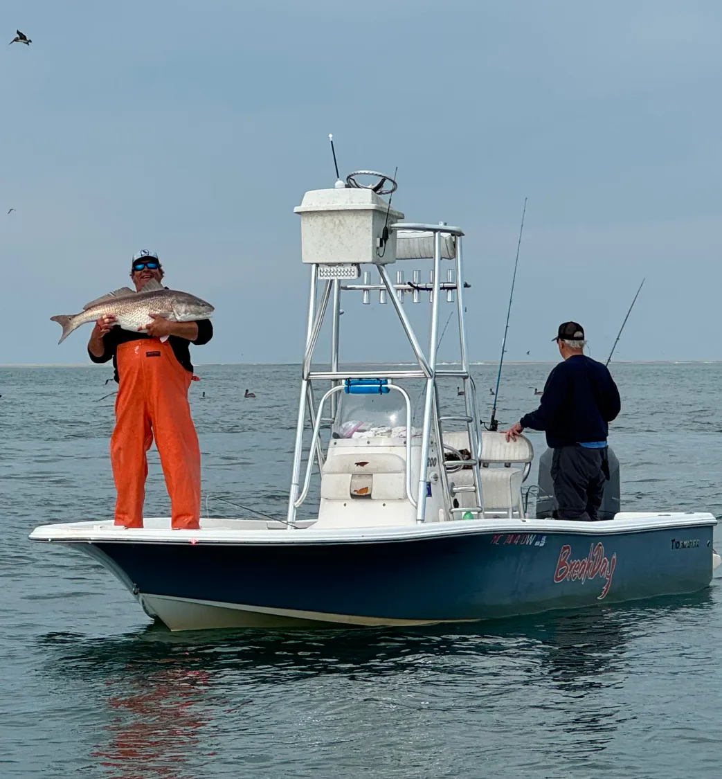 charter-3 Two people fishing on a boat; one holds a large fish, the other stands at the rear with a fishing rod.