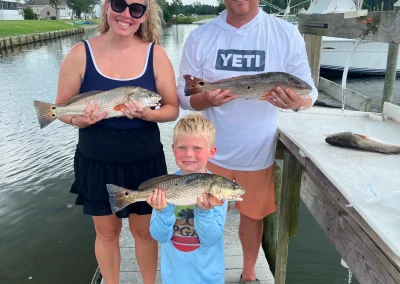 Smiling family holding fish on a dock by the water, with boats and houses in the background.