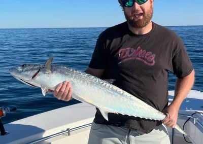 Man in sunglasses proudly holding a large fish on a boat in the ocean under a clear blue sky.