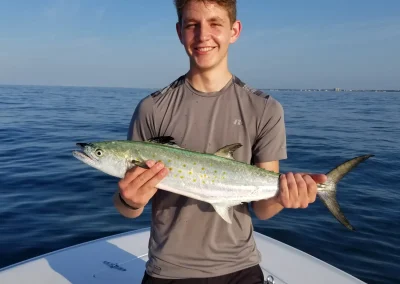 Smiling person on a boat holding a large fish with blue ocean and sky in the background.