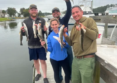 Four smiling people on a dock proudly holding up several freshly caught fish on a cloudy day.