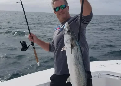 Man on a boat holding a fishing rod and a large fish, with the ocean in the background.