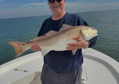 Smiling person on a boat holding a large fish with the ocean and sky in the background.