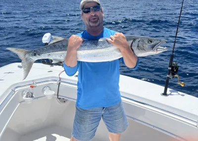 Man in blue shirt holding a large fish on a boat with ocean and cloudy sky in the background.