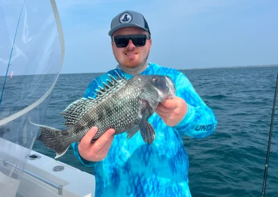 Man in a blue shirt holding a fish on a boat with the ocean in the background.