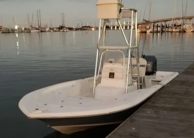 A white fishing boat with a raised tower docked at a marina with sailboats in the background.