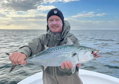 Person standing on a boat holding a large fish, with the ocean and a cloudy sky in the background.