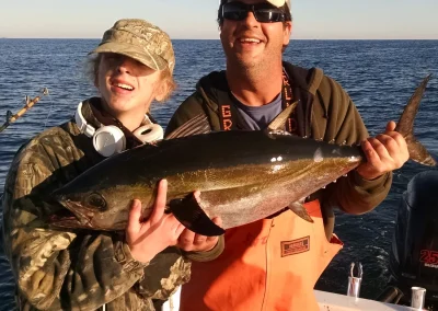 Two people on a boat holding a large fish, smiling with the ocean and blue sky in the background.