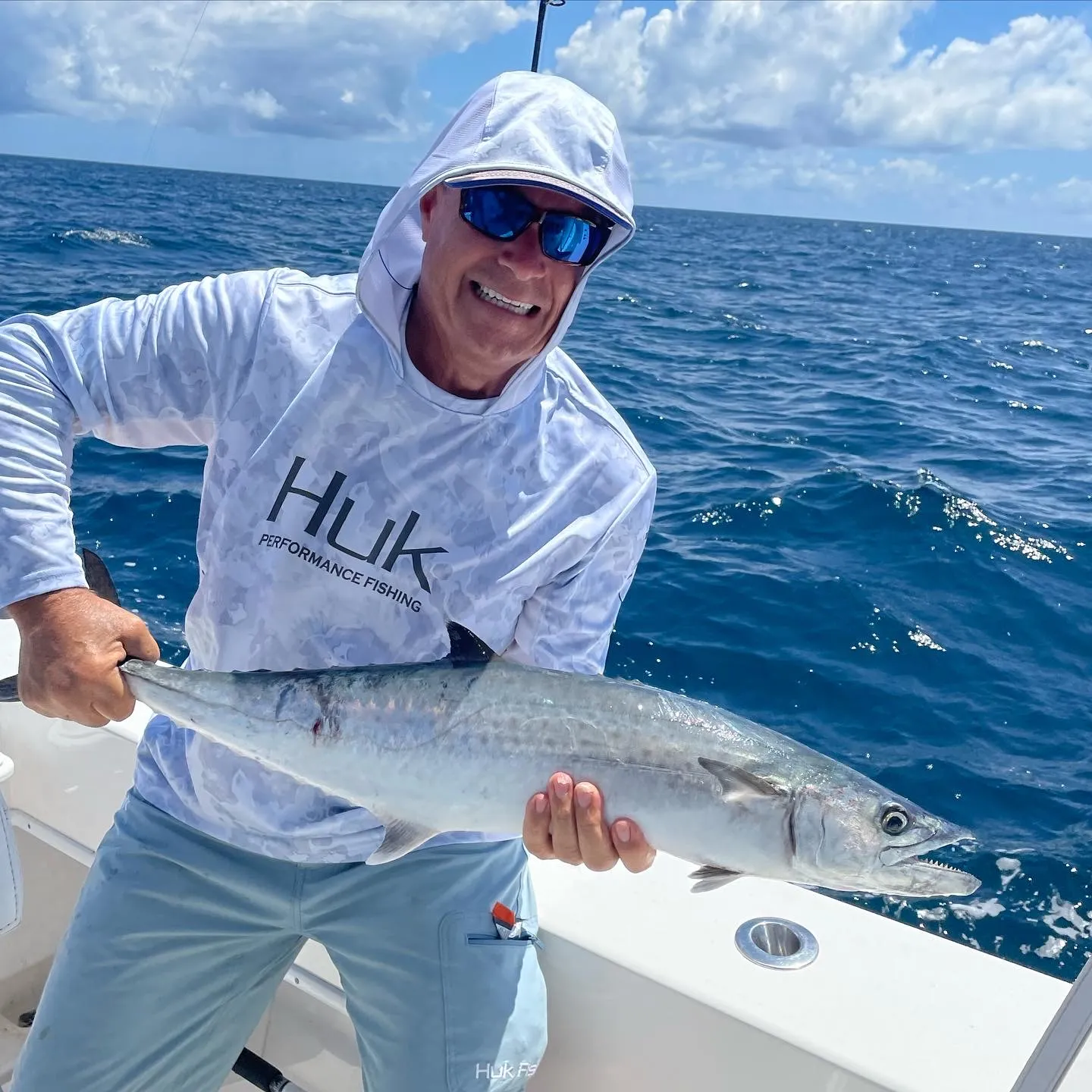 nearshore-2 Smiling person in fishing gear holding a large fish on a boat in the ocean under a partly cloudy sky.