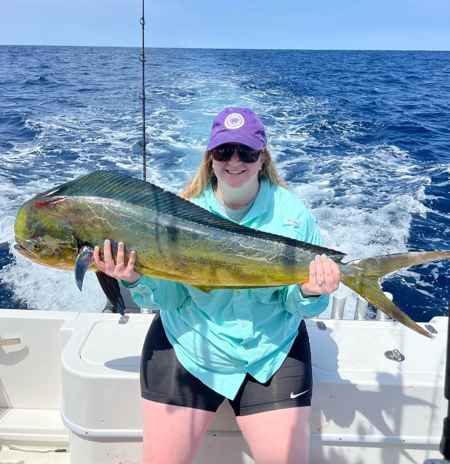 Woman on a boat holding a large mahi-mahi fish, with the ocean and sky in the background.