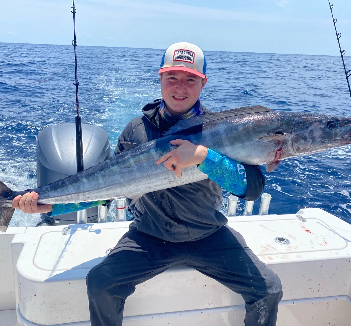 Man sitting on a boat holding a large fish with the ocean in the background.