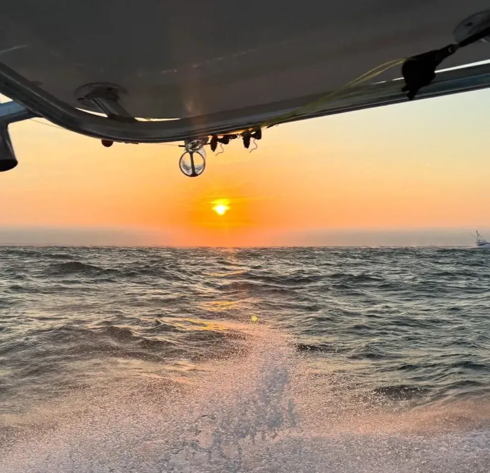 Sunset over the ocean seen from a boat, with water splashing and waves visible.