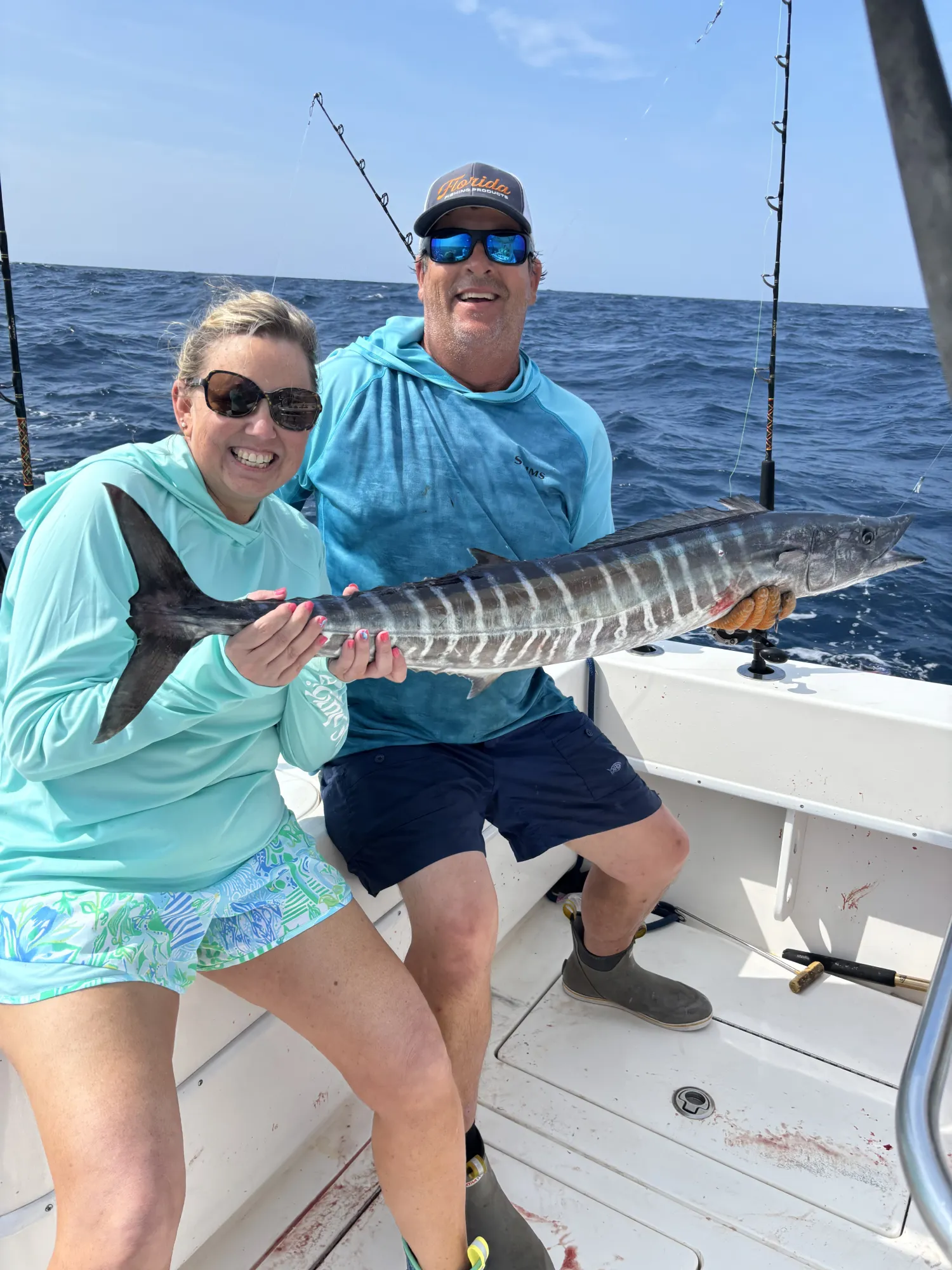 why-choose-1 Two people on a boat smiling and holding a large striped fish with fishing rods in the background.